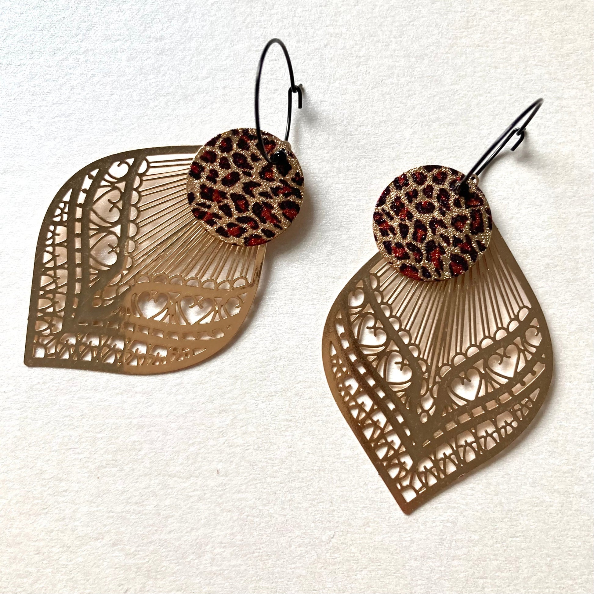 Ohrringe mit kleinen,runden,Leopard Muster Aufhängern und goldfarbenen, filigran geschnittenen Blattformen.