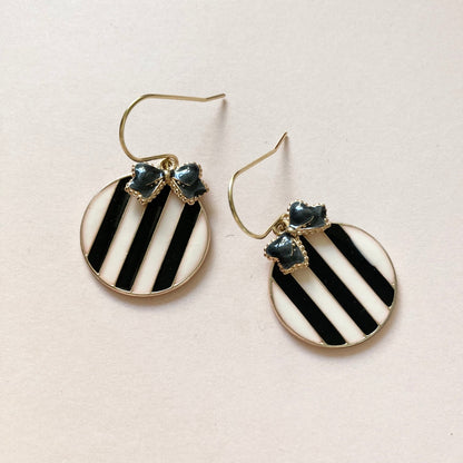 Runde Ohrringe mit schwarz-weißen diagonalen Streifen und kleinen schwarzen Schleifenverzierungen am oberen Rand.