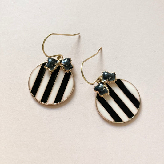 Runde Ohrringe mit schwarz-weißen diagonalen Streifen und kleinen schwarzen Schleifenverzierungen am oberen Rand.