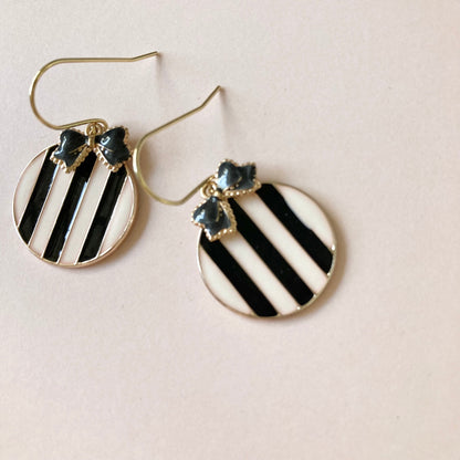 Runde Ohrringe mit schwarz-weißen diagonalen Streifen und kleinen schwarzen Schleifenverzierungen am oberen Rand.