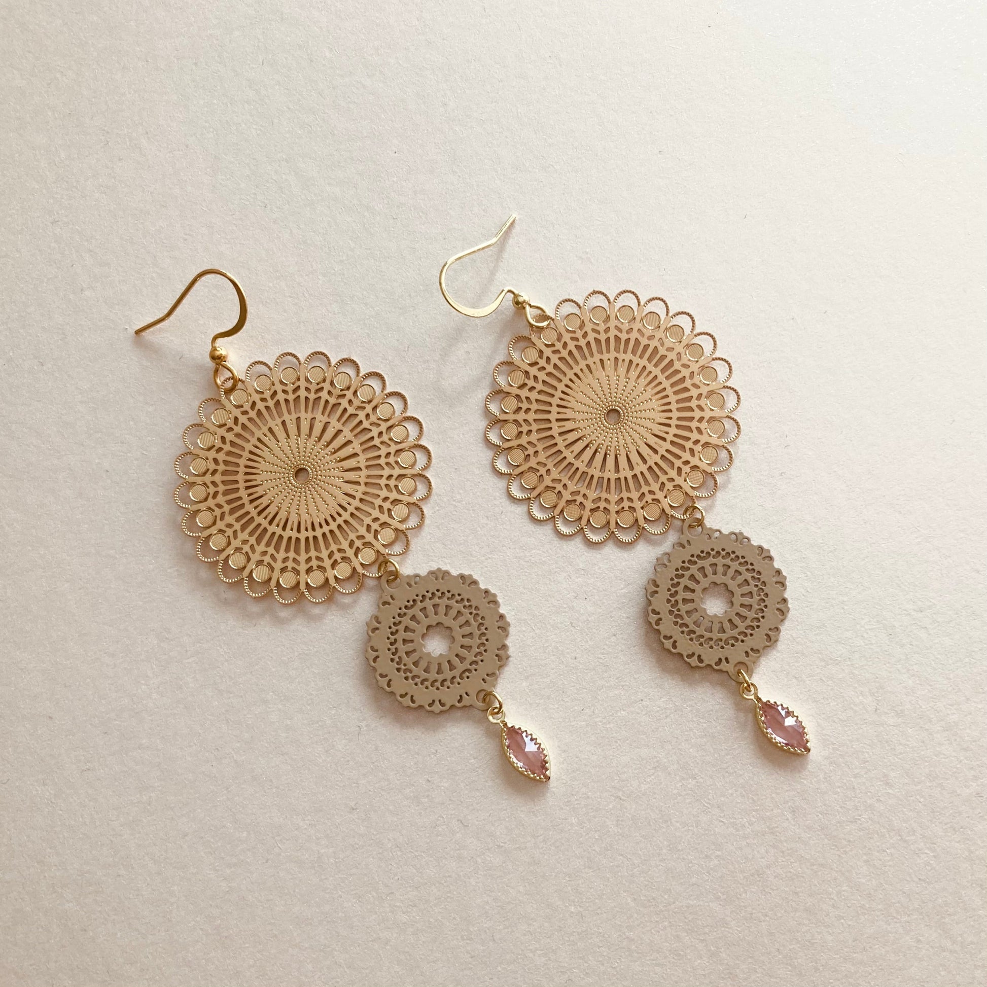 Goldfarbene Ohrringe mit filigranen, runden Mandala-Vebindern und tropfenförmigen, rosafarbenen Anhängern.