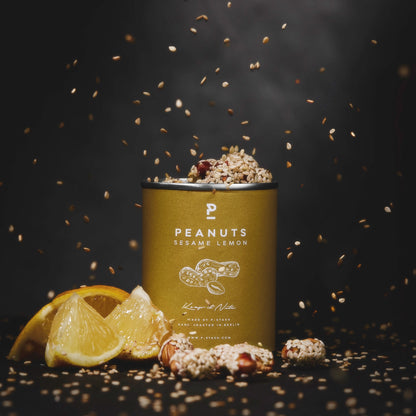 Dose mit Erdnüssen, Sesam und Zitrone, daneben Zitronenscheiben und verstreute Sesamsamen