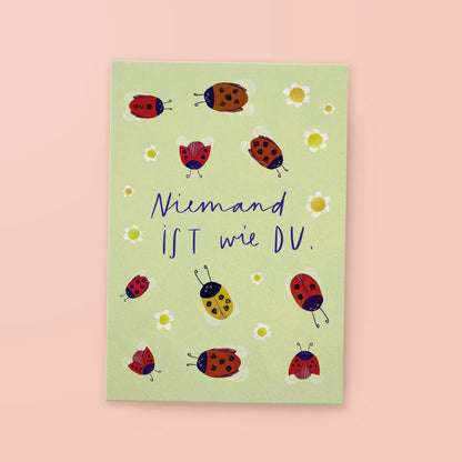 Grüne Karte mit handgeschriebenem Text 'Niemand ist wie DU.' umgeben von Marienkäfern und kleinen weißen Blumen