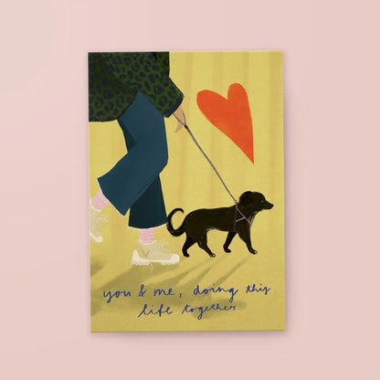 Illustration einer Person in blauer Hose und weißen Schuhen, die einen kleinen schwarzen Hund an der Leine führt, daneben ein rotes Herz und der Text 'you & me, doing this life together'