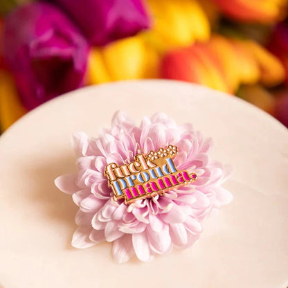 Hellrosa Blüte mit bunter Anstecknadel 'fuck proud mama' auf weißem runden Teller