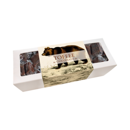 Weiße Schachtel mit durchsichtigen Fenstern, darin mehrere dunkle Toffee-Pralinen, Etikett mit braunem Bären und Schrift 'TOFFEE SCHOKOLADE'.