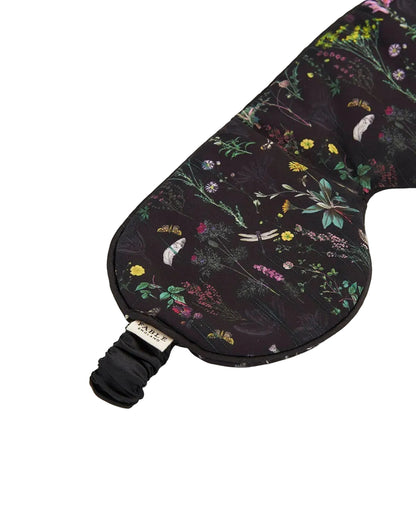 Nahaufnahme einer schwarzen Schlafmaske mit einem Muster aus botanischen Wildblumen und Libellen, verpackt in einem passenden Beutel.