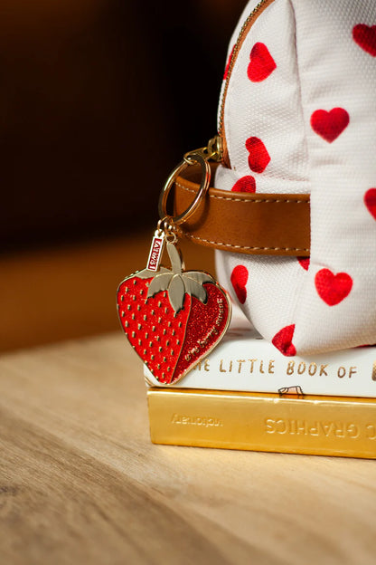 Schlüsselanhänger in Form einer roten Erdbeere an weißer Tasche mit roten Herzen, auf Stapel Bücher