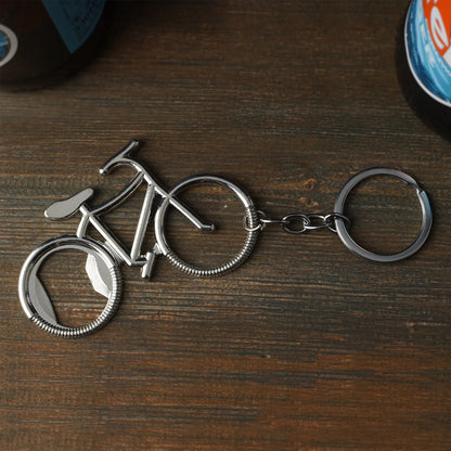 Schlüsselanhänger in Form eines Fahrrads aus Metall mit integriertem Flaschenöffner, auf einem Holztisch liegend