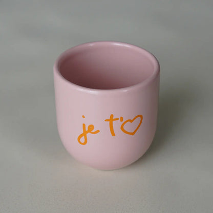 Ein rosa Keramikbecher mit orangefarbener Aufschrift „je taime“.