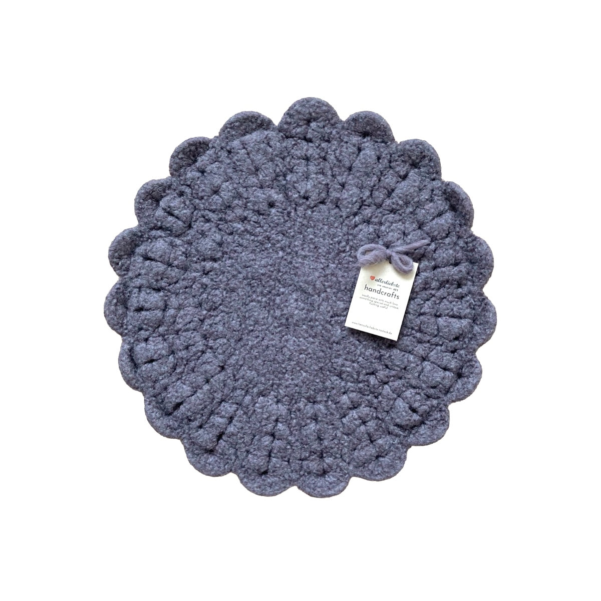 Eine handgehäkelte Sitzunterlage in Borke mit romantischen Blütensaum. Das zentrale Häkelmuster in Kreisform bildet einen harmonischen Kontrast zum verspielten Rand. 