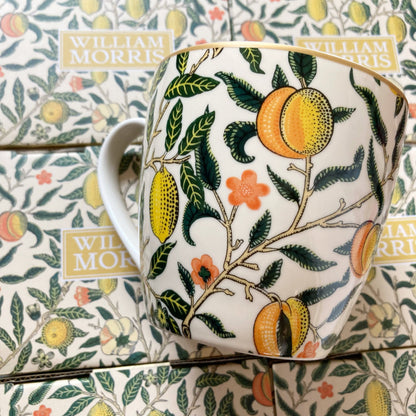 Weißer Keramikbecher mit gelben Zitronen und grünen Blättern als Muster, goldfarbener Rand am oberen Rand.