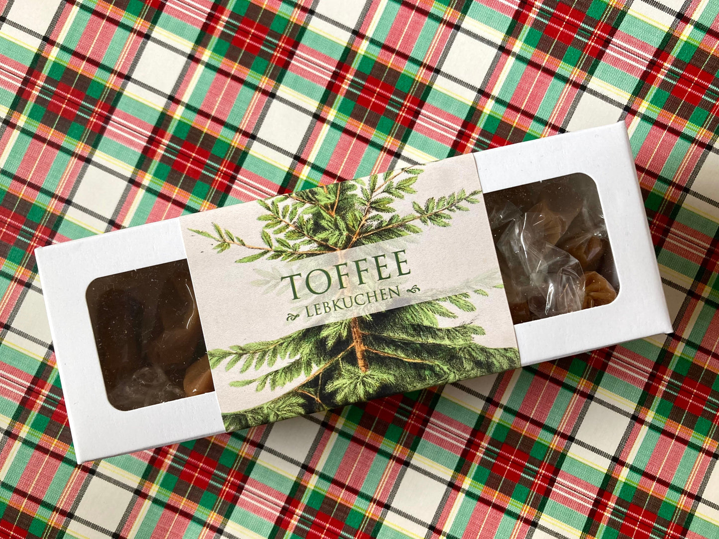 Weiße Schachtel mit Toffee-Karamellbonbons, Etikett mit grünen Tannenzweigen und Schriftzug 'TOFFEE mit LEBKUCHEN'