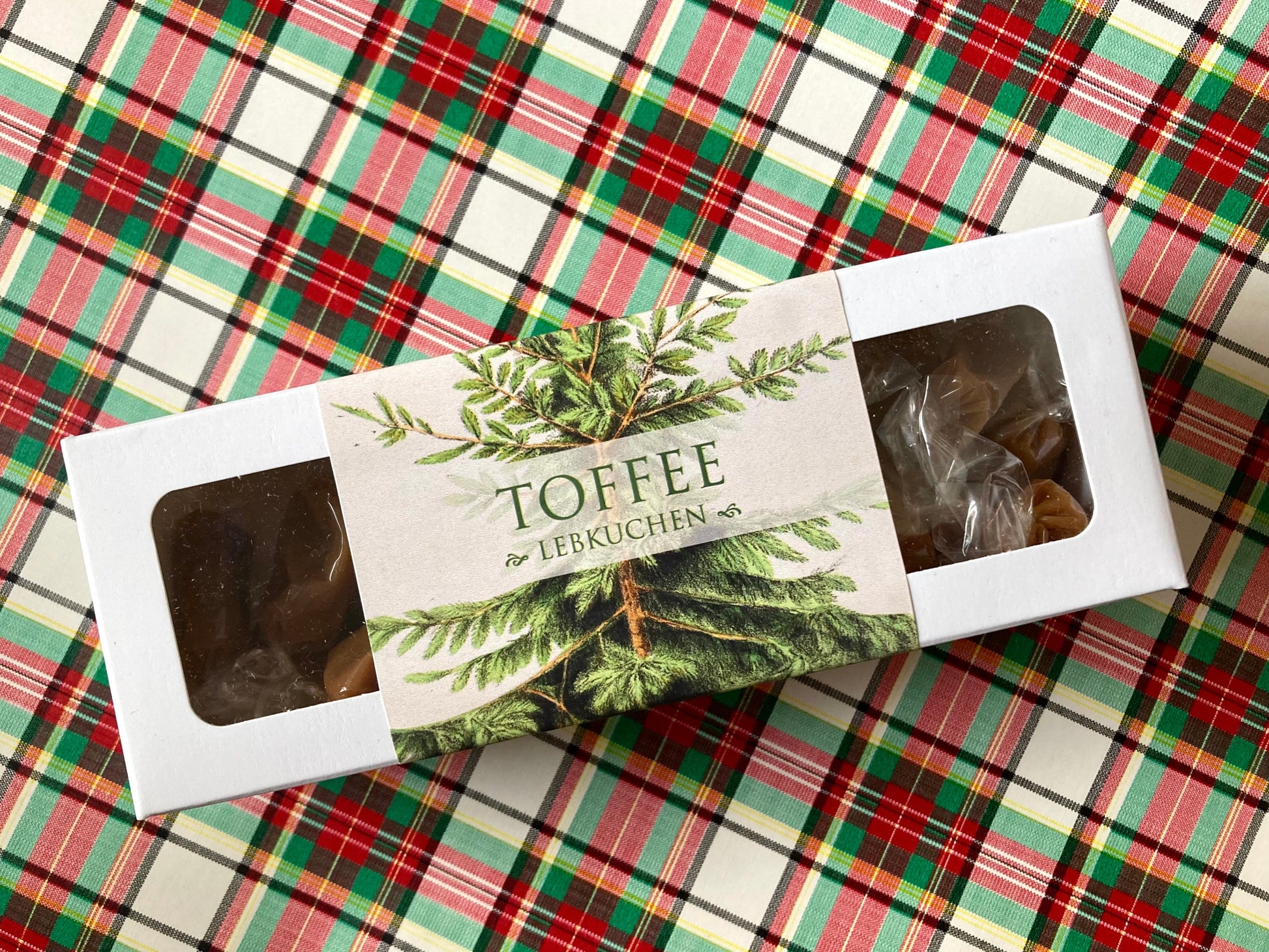 Weiße Schachtel mit Toffee-Karamellbonbons, Etikett mit grünen Tannenzweigen und Schriftzug 'TOFFEE mit LEBKUCHEN'