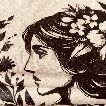 Beige Stofftasche mit schwarzem Druck einer Frau mit langem Haar, umgeben von Blumen und Blättern, darunter Schriftzug 'MOOIS'