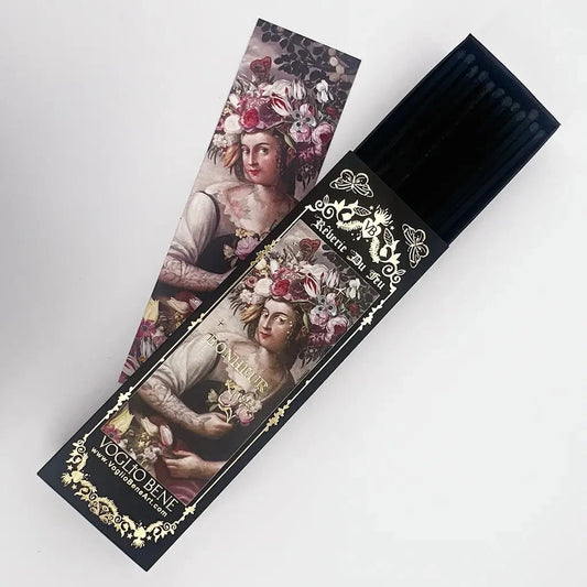 Schwarze Verpackung mit goldener Verzierung und Text 'Reverie Du Feu' enthält schwarze Streichhölzer, daneben eine Karte mit einem Porträt einer Frau mit Blumen im Haar