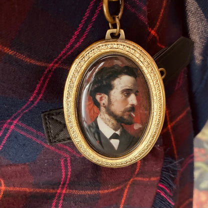 Ovaler goldener Medaillonanhänger mit einem Porträt eines Mannes in schwarzem Anzug und weißem Hemd