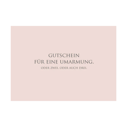 Dieses Bild zeigt eine  Postkarte mit deutschem Text auf rosafarbenem Hintergrund. Die Karte enthält grauen Text in einer klaren, modernen Schriftart mit der folgender Botschaft: „GUTSCHEIN FÜR EINE UMARMUNG. ODER ZWEI. ODER AUCH DREI.“