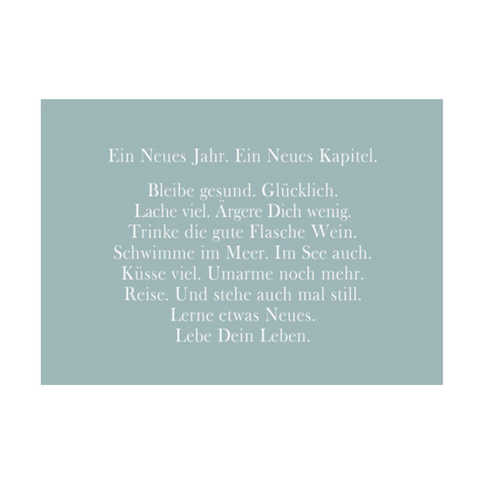 Blaugraue Postkarte mit weißer Schrift und dem Text: "Ein Neues Jahr. Ein Neues Kapitel. Bleibe gesund. Glücklich. Lache viel. Ärgere Dich wenig. Trinke die gute Flasche Wein. Schwimme im Meer. Im See auch. Küsse viel. Umarme noch mehr. Reise. Und stehe auch mal still. Lerne etwas Neues. Lebe Dein Leben."