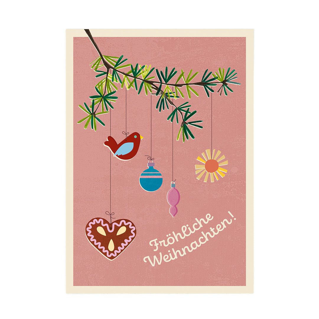 Eine illustrative Weihnachtskarte auf einem altrosa Hintergrund mit einem Tannenzweig oben links. An Schnüren hängen ein kleiner blauer Vogel, ein blaues und ein rosa Ornament, eine kleine gelbe Sonne und ein Lebkuchenherz . Unten rechts steht in geschwungener Schrift „Fröhliche Weihnachten!