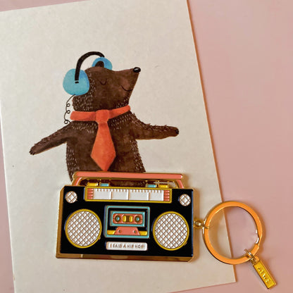Schlüsselanhänger in Form eines schwarzen Ghettoblasters mit Aufschrift 'I SAID A HIP HOP' vor einer Zeichnung eines Bären mit roter Krawatte und blauen Kopfhörern
