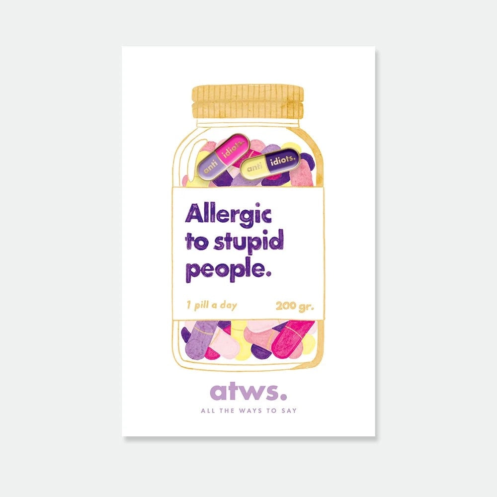 Zwei Emaille-Pins in Pillenform (lila/pink und gelb/dunkelblau) mit der Aufschrift „anti idiots“ auf einer Trägerkarte, die ein Glas mit der Aufschrift „Allergic to stupid people“ zeigt.