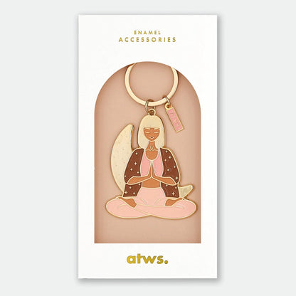 Schlüsselanhänger mit einer sitzenden Frau in Meditationshaltung, Hände vor der Brust gefaltet, trägt ein braunes Oberteil und rosa Hose