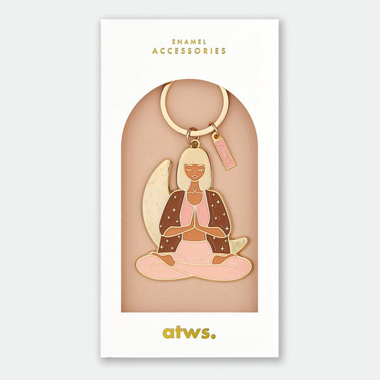 Schlüsselanhänger mit einer sitzenden Frau in Meditationshaltung, Hände vor der Brust gefaltet, trägt ein braunes Oberteil und rosa Hose