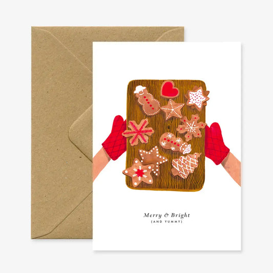 Backblech mit verschiedenen Lebkuchen in Stern-, Herz-, Tannenbaum- und Schneemannformen, gehalten von Händen mit roten Ofenhandschuhen.