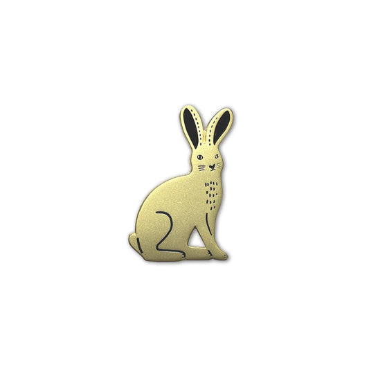 Detailaufnahme eines goldfarbenen Emaille-Pins in Form eines sitzenden Feldhasen mit schwarzen Akzenten an den Ohren und minimalistischen grafischen Details