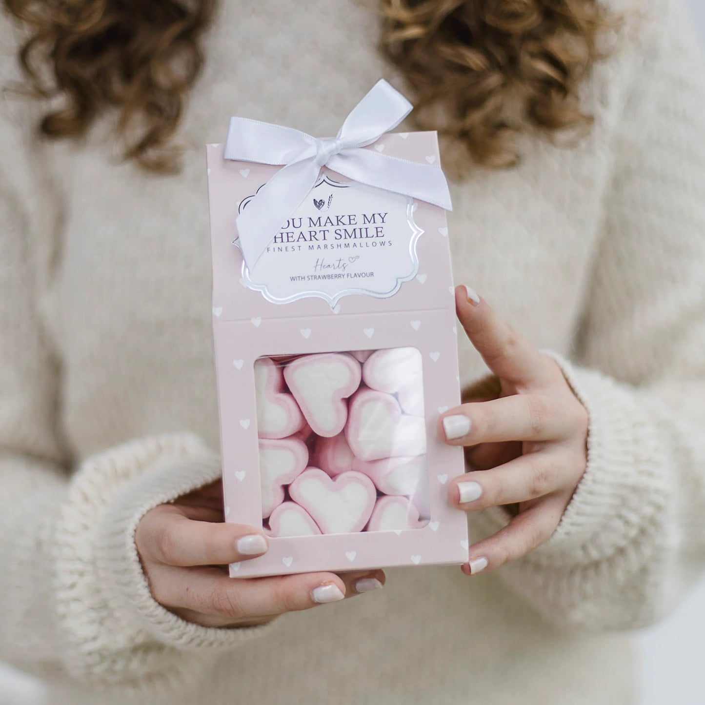 Eine Person hält eine Geschenkpackung mit herzförmigen Erdbeer-Marshmallows.