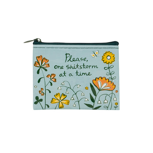 Eine hellblaue Geldbörse, die mit verschiedenen illustrierten Blumen und einem kleinen Schmetterling verziert ist. In der Mitte steht der handgeschriebene Text: „Please, one Shitstorm at a time.“
