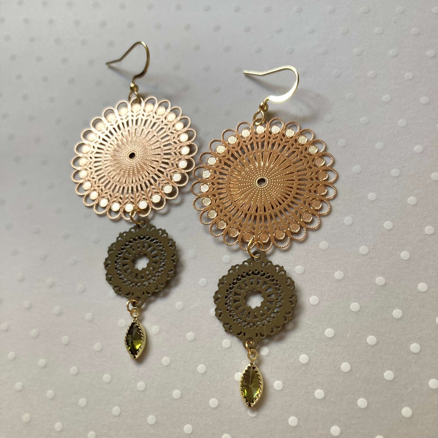 Goldfarbene Ohrringe mit filigranen, runden Mandala-Vebindern und tropfenförmigen, olivgrünen Anhängern.