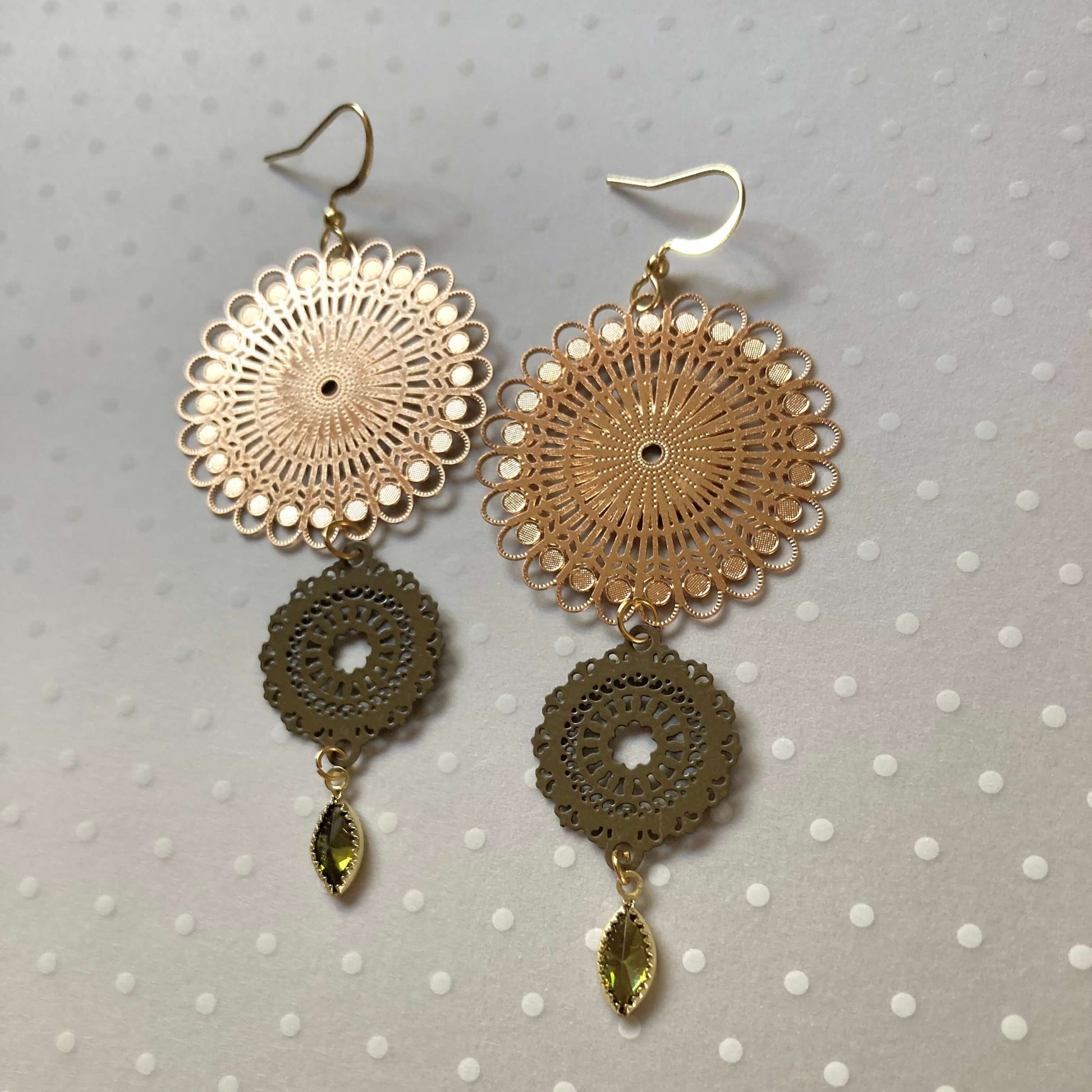 Goldfarbene Ohrringe mit filigranen, runden Mandala-Vebindern und tropfenförmigen, olivgrünen Anhängern.