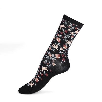 Ein Paar schwarze Maison Broussaud Socken mit Allover-Print aus kleinen Erdbeeren und Vögeln und grünen Blättern, flach auf weißem Hintergrund präsentiert.