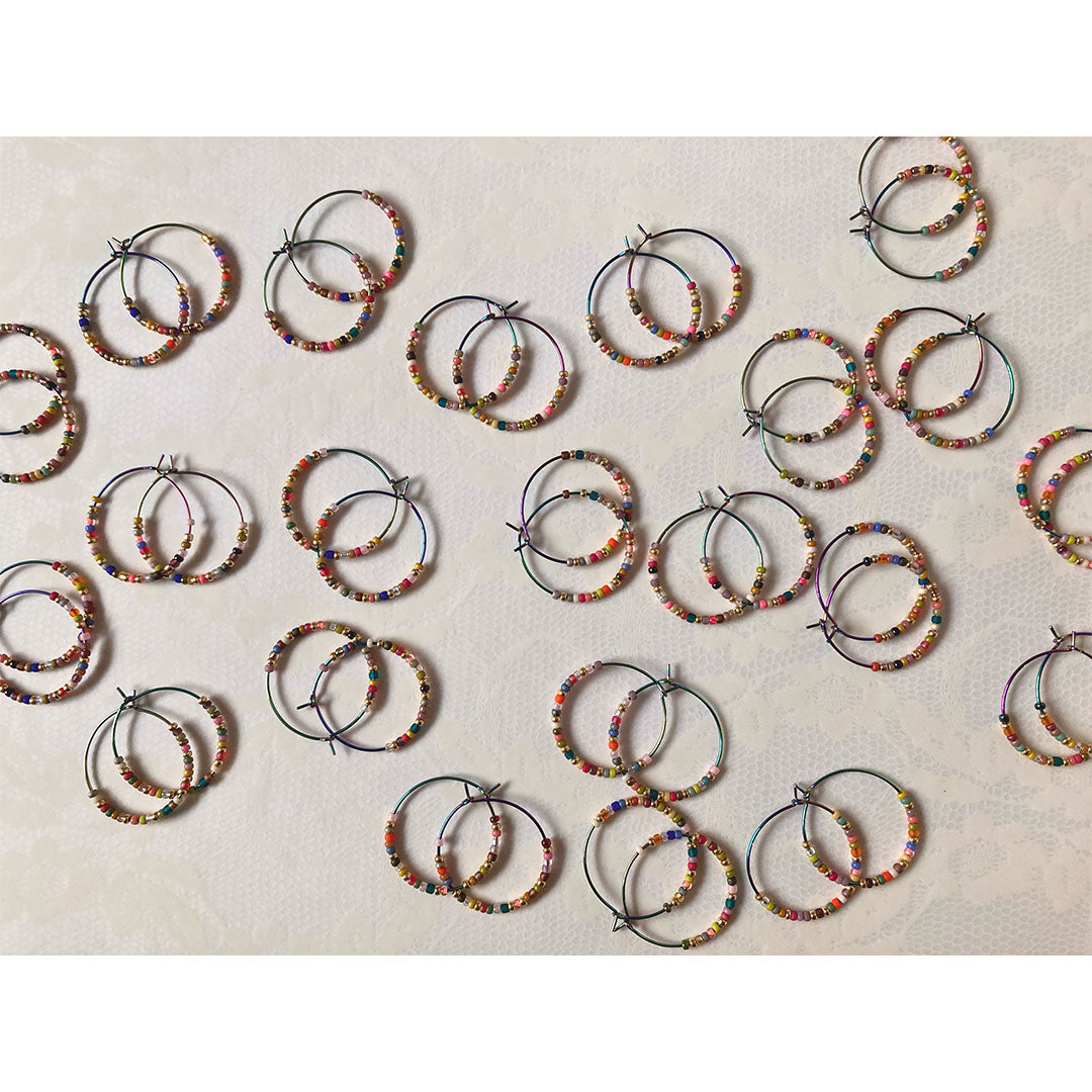 Bunte Perlen-Creolen in verschiedenen Farben auf einem hellen Untergrund. Die handgefertigten Ohrringe zeigen eine bunte Mischung aus Glasperlen und metallischen Akzenten an regenbogenfarbenen Metallreifen.