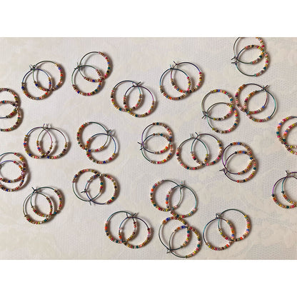 Bunte Perlen-Creolen in verschiedenen Farben auf einem hellen Untergrund. Die handgefertigten Ohrringe zeigen eine bunte Mischung aus Glasperlen und metallischen Akzenten an regenbogenfarbenen Metallreifen.