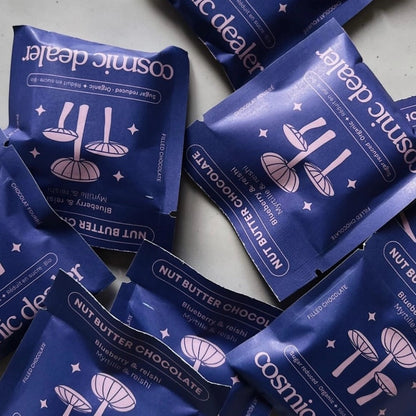 Mehrere einzeln verpackte Cosmic Dealer Nut Butter Schokoriegel im 16er-Pack verstreut.