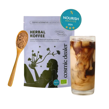Produktpräsentation der Kaffealternative „Herbal Koffee“ von Cosmic Dealer. Links steht ein Holzlöffel voller feinem, braunem Pulver, in der Mitte die hellviolette Verpackung und rechts ein hohes, transparentes Glas mit einem Eiskaffee-Mischgetränk aus dunklem Kaffee und heller Milch. Oben rechts glänzt ein blaues „Nourish Awards 2024“-Siegel.