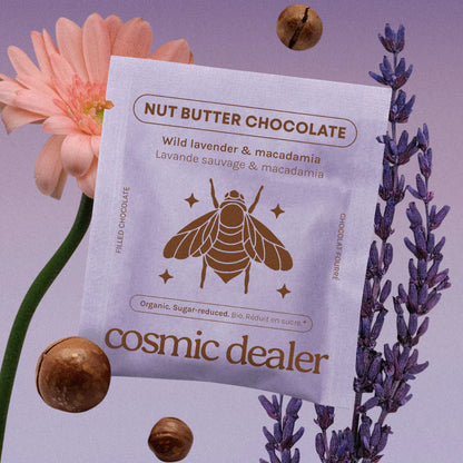 Cosmic Dealer Verpackung der Schokolade Wild Lavender & Macadamia in Zartviolett mit Bienen-Illustration, schwebenden Macadamianüssen und frischem Lavendel.