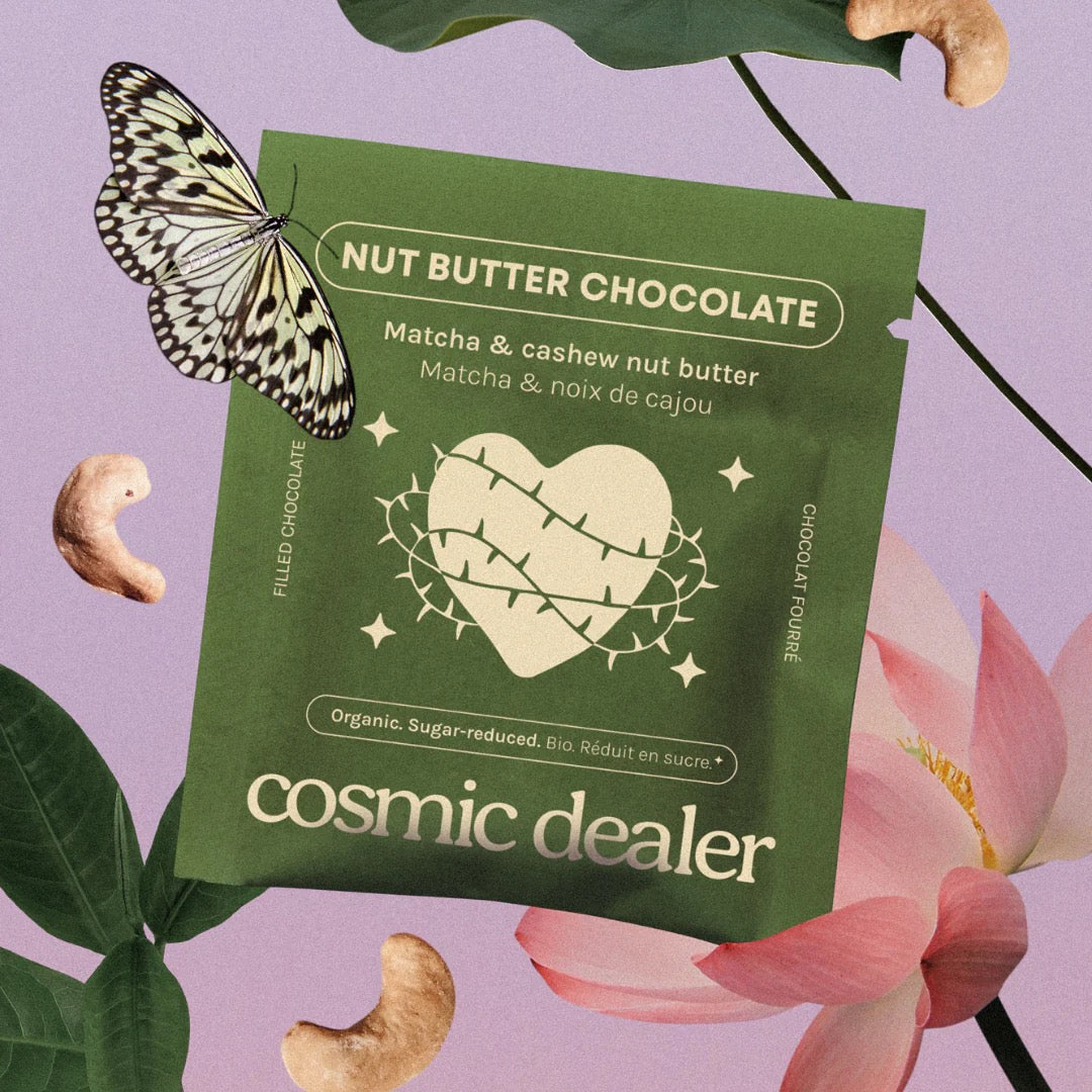 Verpackung der Cosmic Dealer Matcha & Cashew Schokolade umgeben von einer Lotusblüte, Cashewnüssen und einem Schmetterling.
