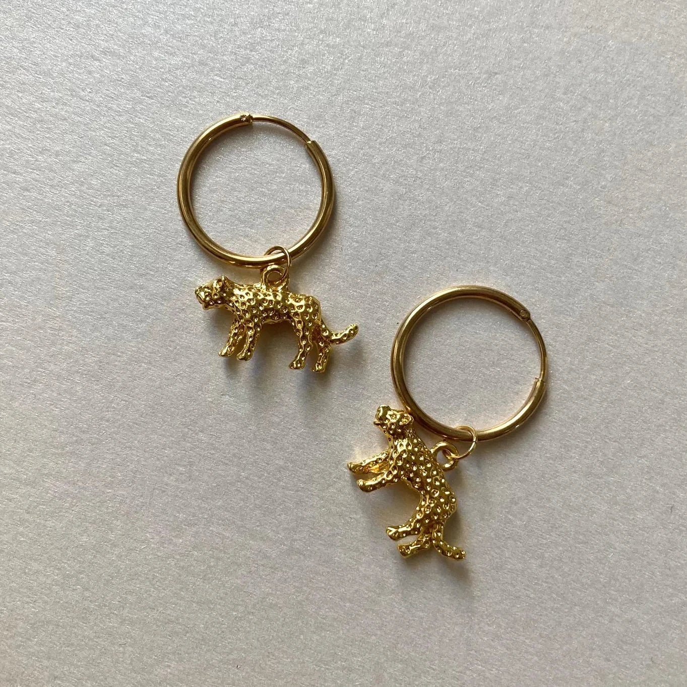 Goldfarbene Creolen mit kleinen, strukturierten Leopard-Anhängern in 3d-Optik.