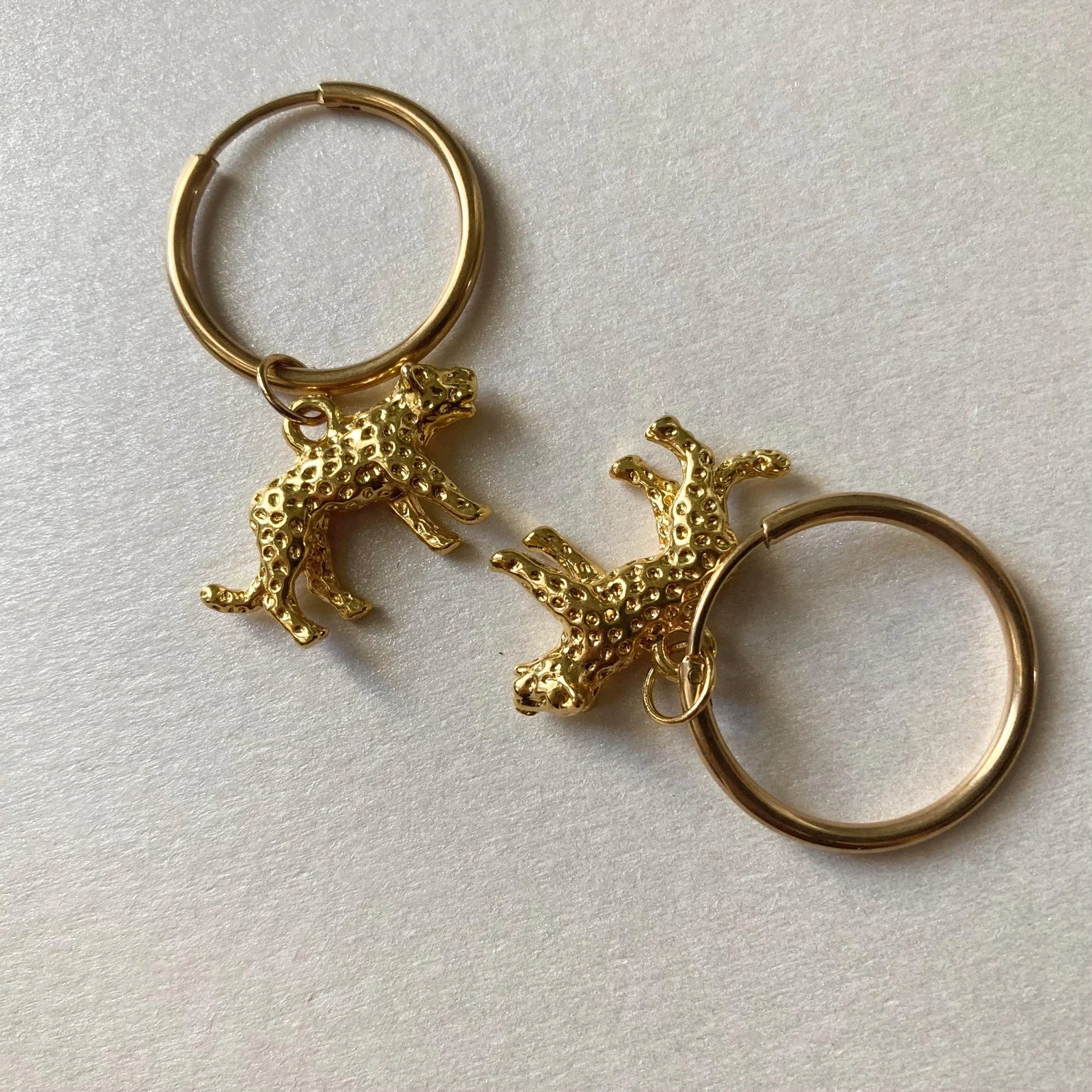 Goldfarbene Creolen mit kleinen, strukturierten Leopard-Anhängern in 3d-Optik.