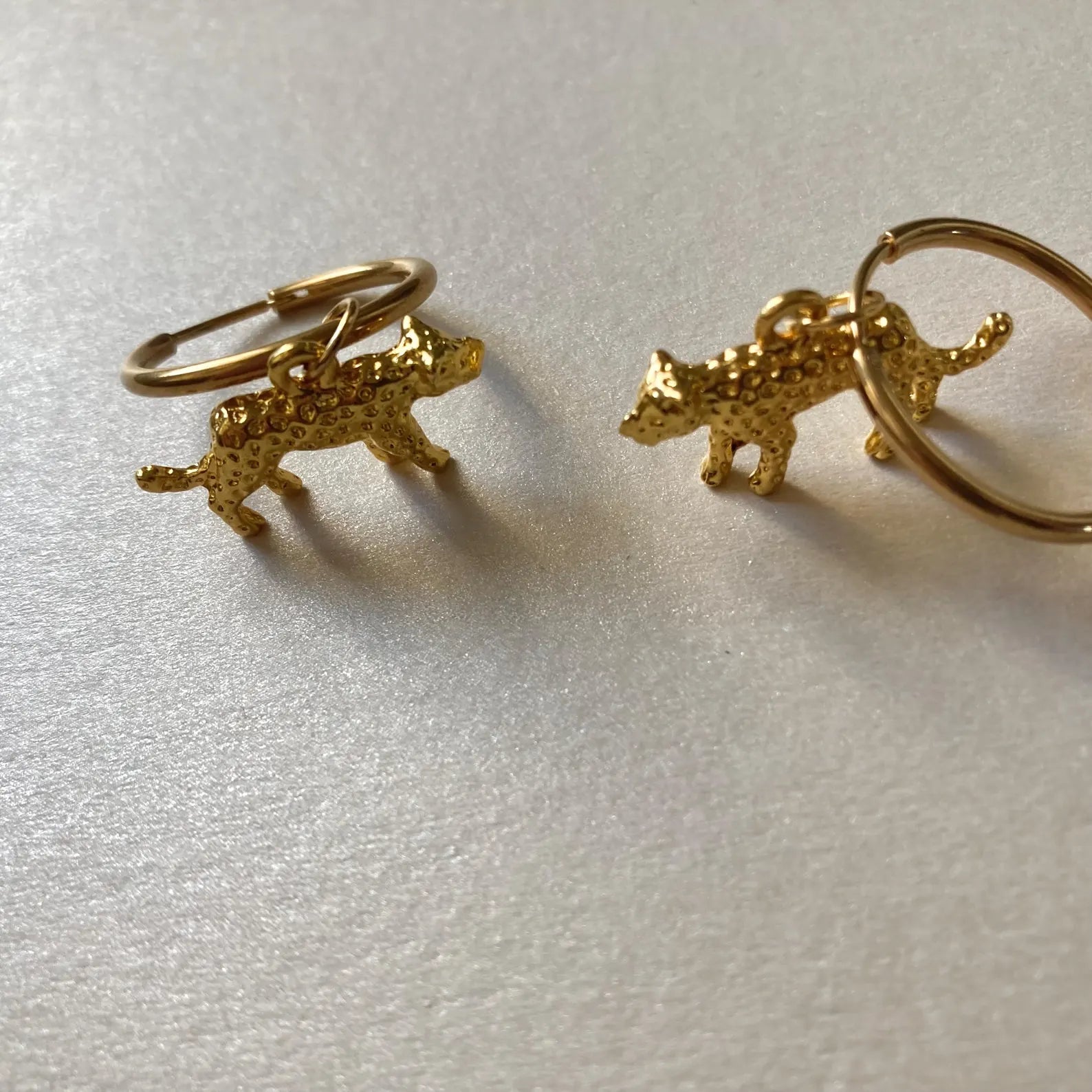 Goldfarbene Creolen mit kleinen, strukturierten Leopard-Anhängern in 3d-Optik.