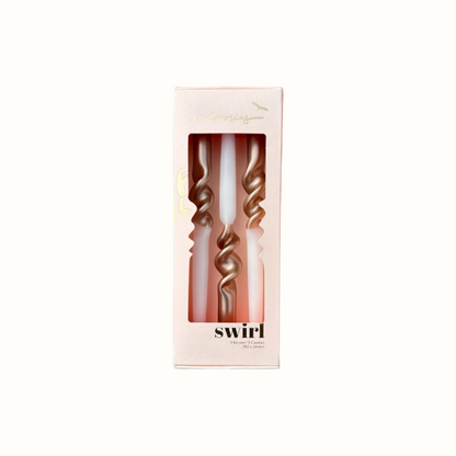 Drei goldfarbene, spiralförmige Kerzen in einer hellrosa Verpackung mit Sichtfenster und der Aufschrift 'swirl'.