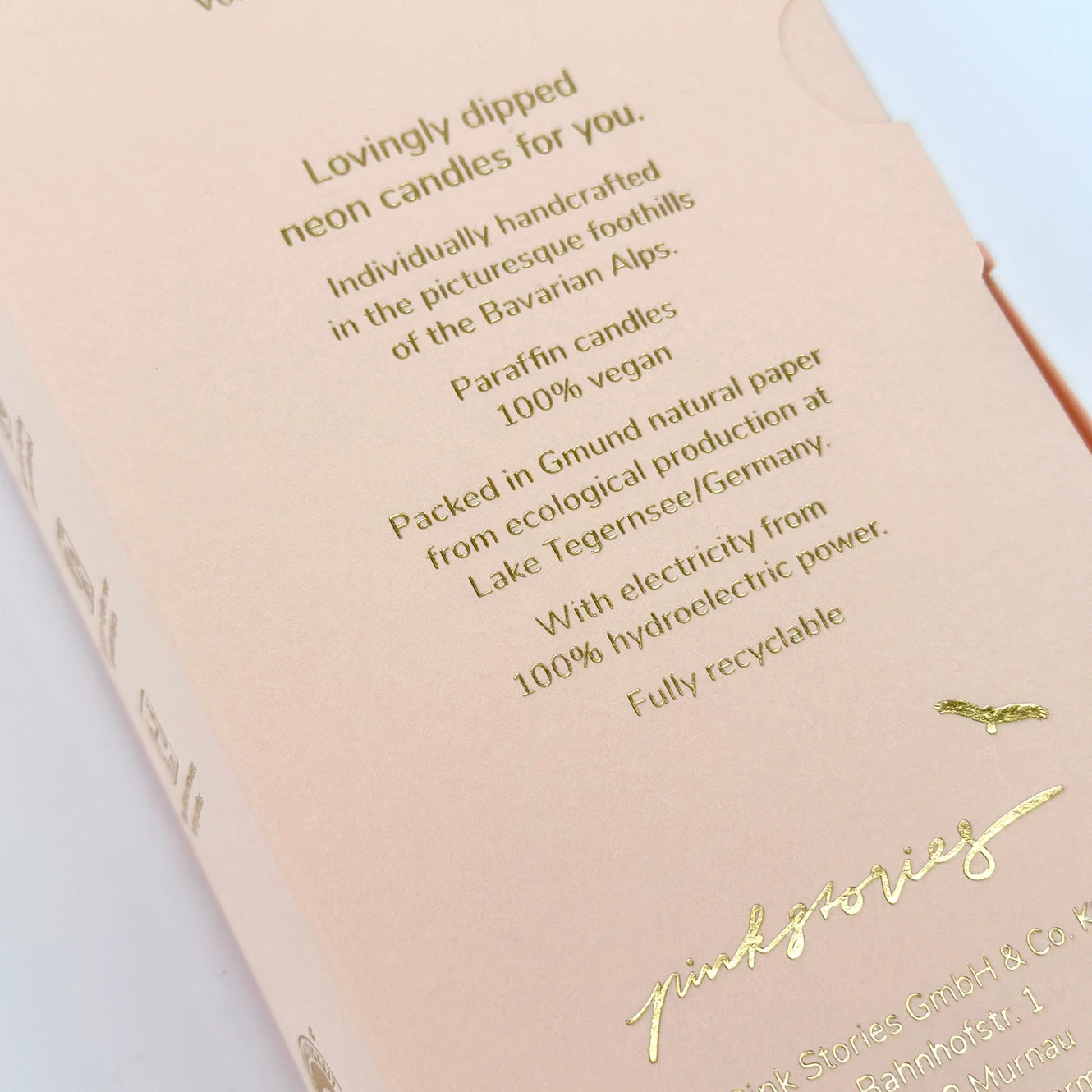 Text auf Verpackung: 'Lovingly dipped neon candles for you. Individually handcrafted in the picturesque foothills of the Bavarian Alps. Paraffin candles 100% vegan. Packed in Gmund natural paper from ecological production at Lake Tegernsee/Germany. With electricity from 100% hydroelectric power. Fully recyclable.'