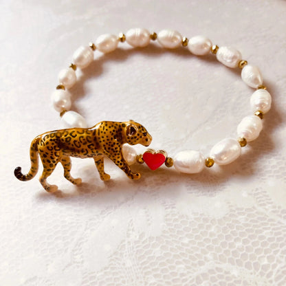 Armband mit weißen Perlen, goldfarbenen Zwischenstücken und einem Leopardenanhänger, der ein pinkes Herz hält.