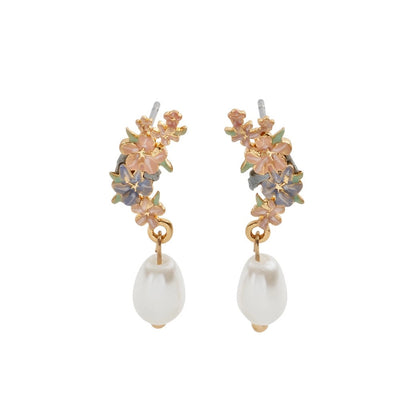 Ein Paar goldfarbene Ohrstecker mit detaillierten, handbemalten Emaille-Blüten in Rosa und Blau, an denen jeweils eine weiße, tropfenförmige Perle hängt. Die Ohrringe sind symmetrisch nebeneinander vor weißem Hintergrund angeordnet.
