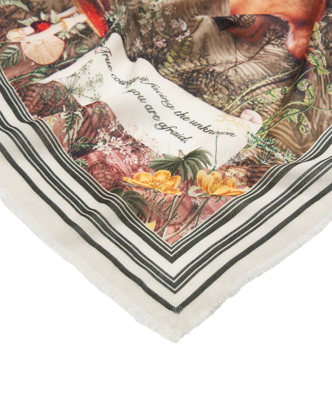 Nahaufnahme einer Ecke des Fable England Schals mit feinen Fransen, gestreifter Bordüre und dem Teil des Zitats „facing the unknown when you are afraid.“ neben einer gelben Blume.