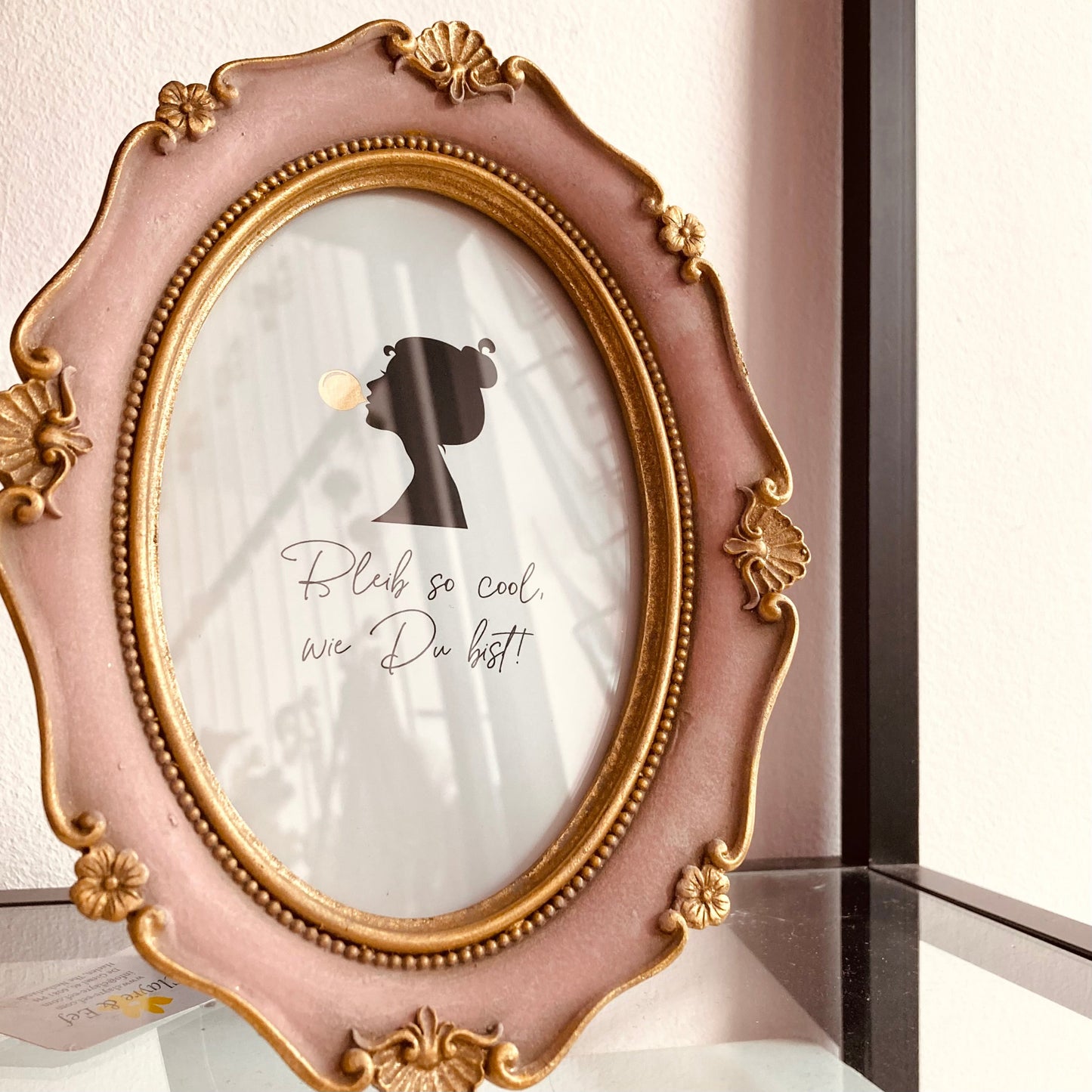 Detailaufnahme eines barocken Fotorahmens in Rosa-Gold mit Silhouette-Grafik und dem Spruch „Bleib so cool, wie Du bist“.